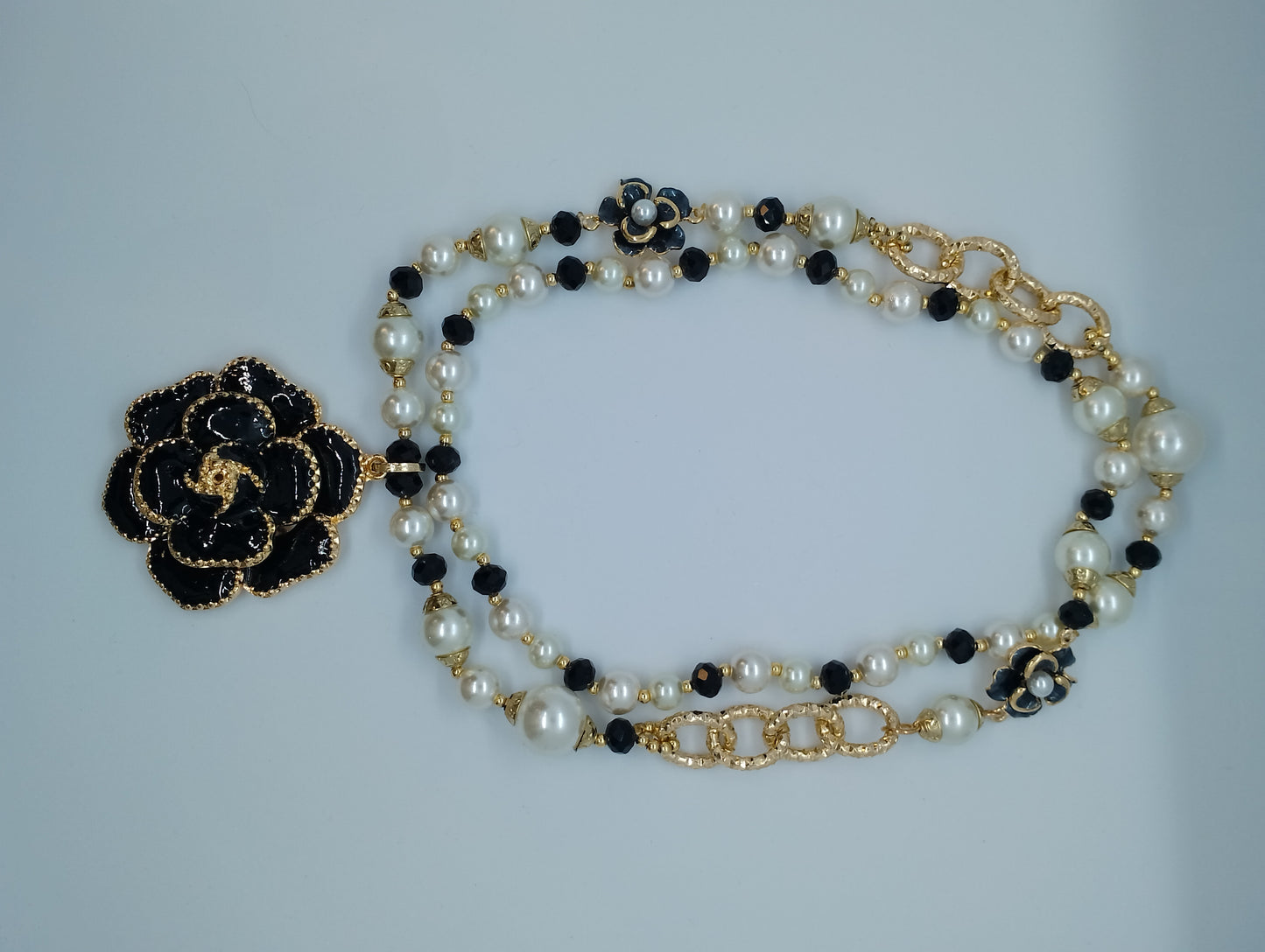 <ul> <li>Collier en perle blanche et noire, sans nickel et de couleur dorée<br></li> <li>Composé d'une fleur en son centre et d'autres fantaisies sur le long des perles<br></li> <li>Le collier est non réglable car ne possède pas de fermoir (photo non contractuelle - le collier ne peut être utilisé comme sur les photos 1 et 3, mais uniquement comme sur la photo 2)</li> <li>Longueur : 45cm et fleur de 5cm</li> </ul>