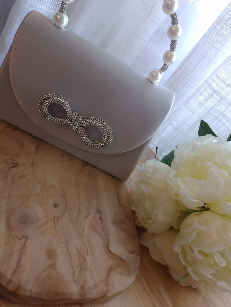 Sac Perla noir nœud strass posé au sol, fond blanc et parquet, pochette soirée femme BONITALUZ