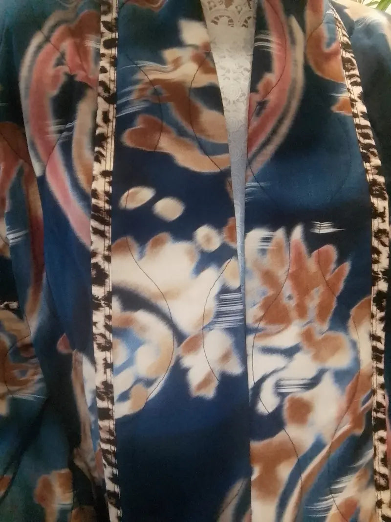 Gros plan de la veste bleu foncé : motifs floraux roses et crème et bordures décoratives contrastées.