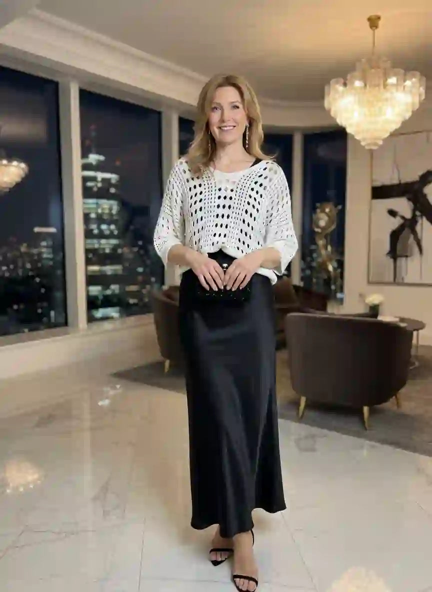 Pull femme blanc crochet ajouré jupe longue satin noire escarpins noirs salon luxe moderne lustre cristal baie vitrée vue ville nocturne look soirée glamour BONITALUZ